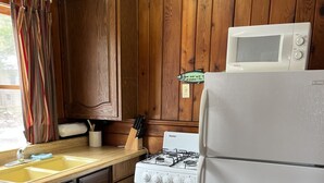 A kitchen with wooden cabinets, a stove, a microwave, and a refrigerator. - Sleeping Bear Riverside Cabins - Cabin #3 (Honor)