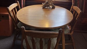 A round wooden table with a lamp and antler decoration, surrounded by wooden chairs, in a room with wooden paneled walls and a window with curtains. - Sleeping Bear Riverside Cabins - Cabin #3 (Honor)