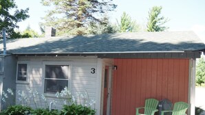 A small house with a number 3 on the door, a porch with two green chairs, and a garden with white flowers. - Sleeping Bear Riverside Cabins - Cabin #3 (Honor)