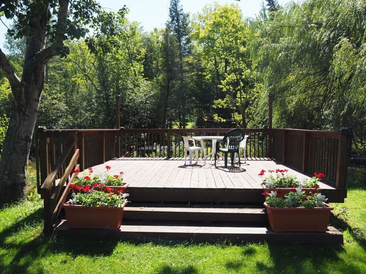 A wooden deck with a table and chairs, surrounded by potted plants and a wooden railing.