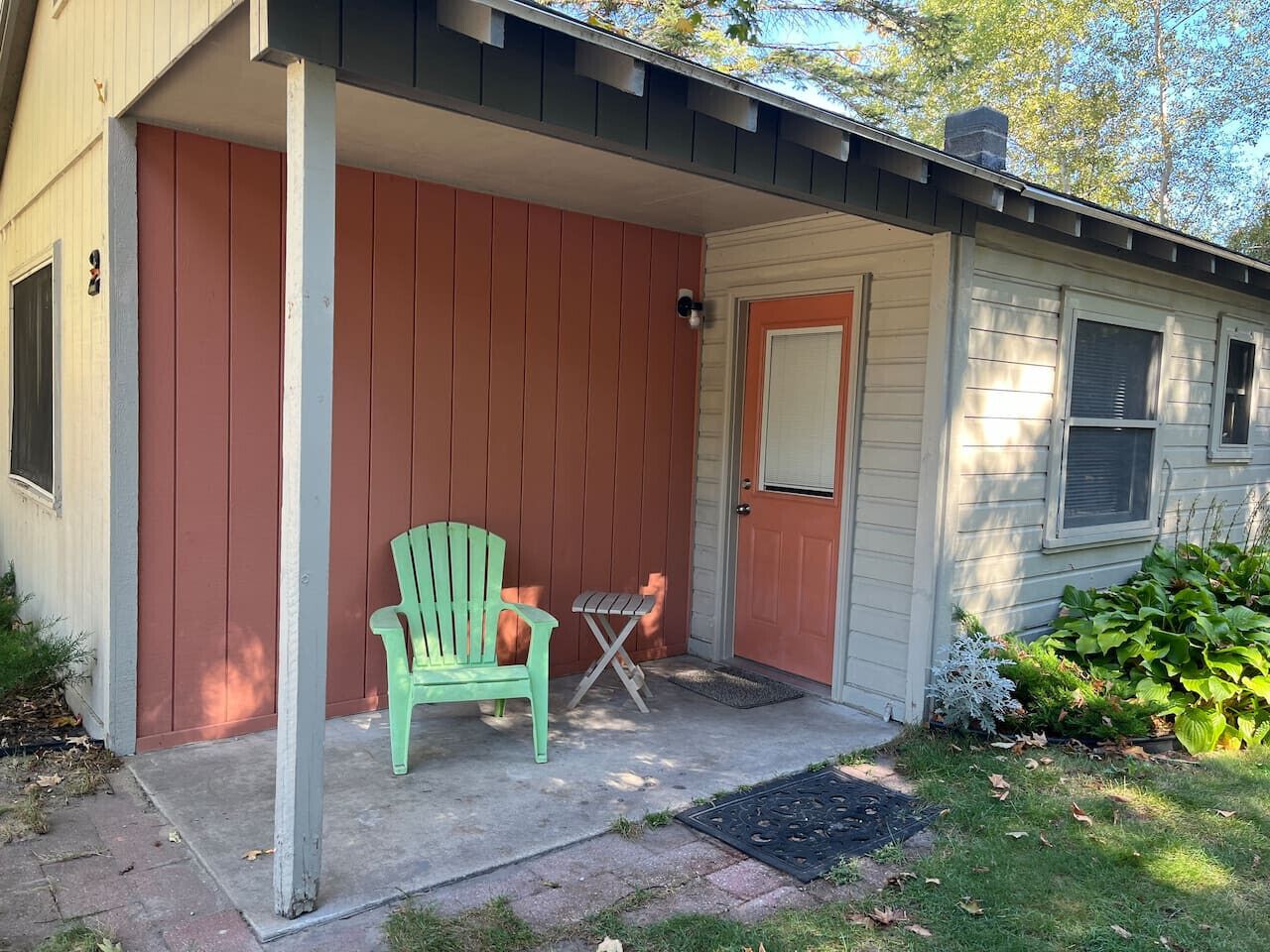 A small house with a porch, a green chair, and a small table.