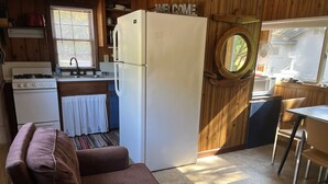 A compact kitchen with a refrigerator, stove, sink, and a dining area with a table and chairs. - Sleeping Bear Riverside Cabins - Cabin #1 (Honor)