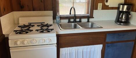 Una cocina compacta con estufa a gas, un lavamanos y una cafetera.