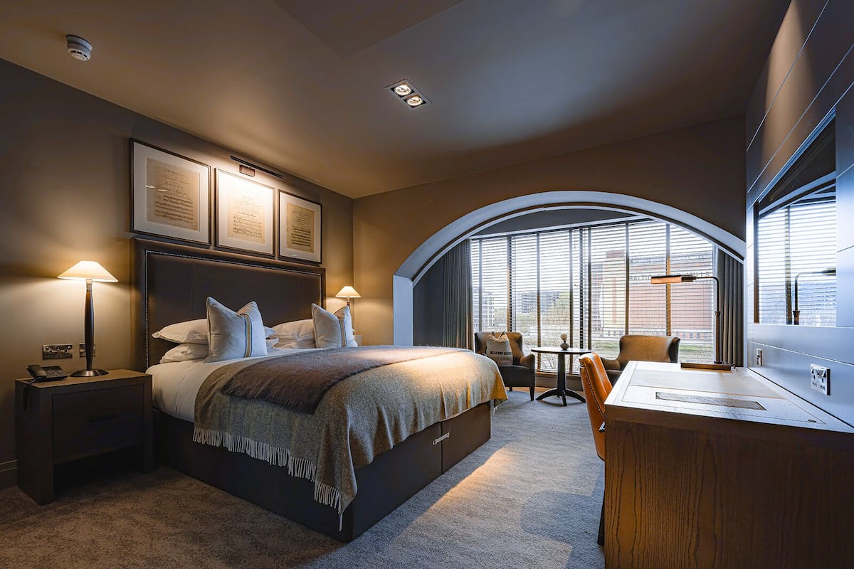 Una habitación de hotel moderna con una cama grande, un escritorio y vistas de la ciudad a través de amplias ventanas.