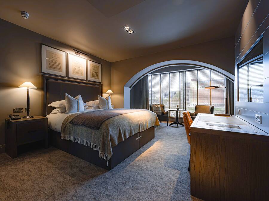 Una habitación de hotel moderna con una cama grande, un escritorio y vistas de la ciudad a través de amplias ventanas.