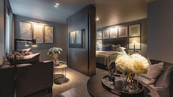 A modern living room with a sofa, a coffee table with a vase of flowers, and a bed with a headboard.