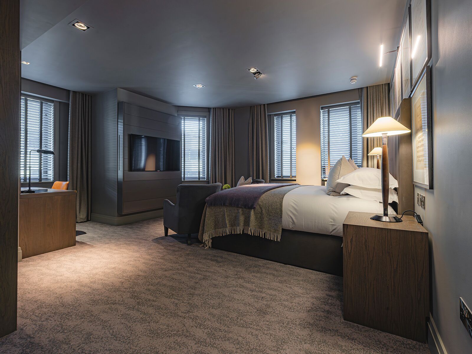 A modern hotel room with a large bed, a desk, a flat-screen TV, and a bedside lamp.