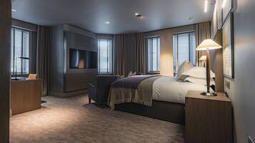 A modern hotel room with a large bed, a desk, a flat-screen TV, and a bedside lamp.