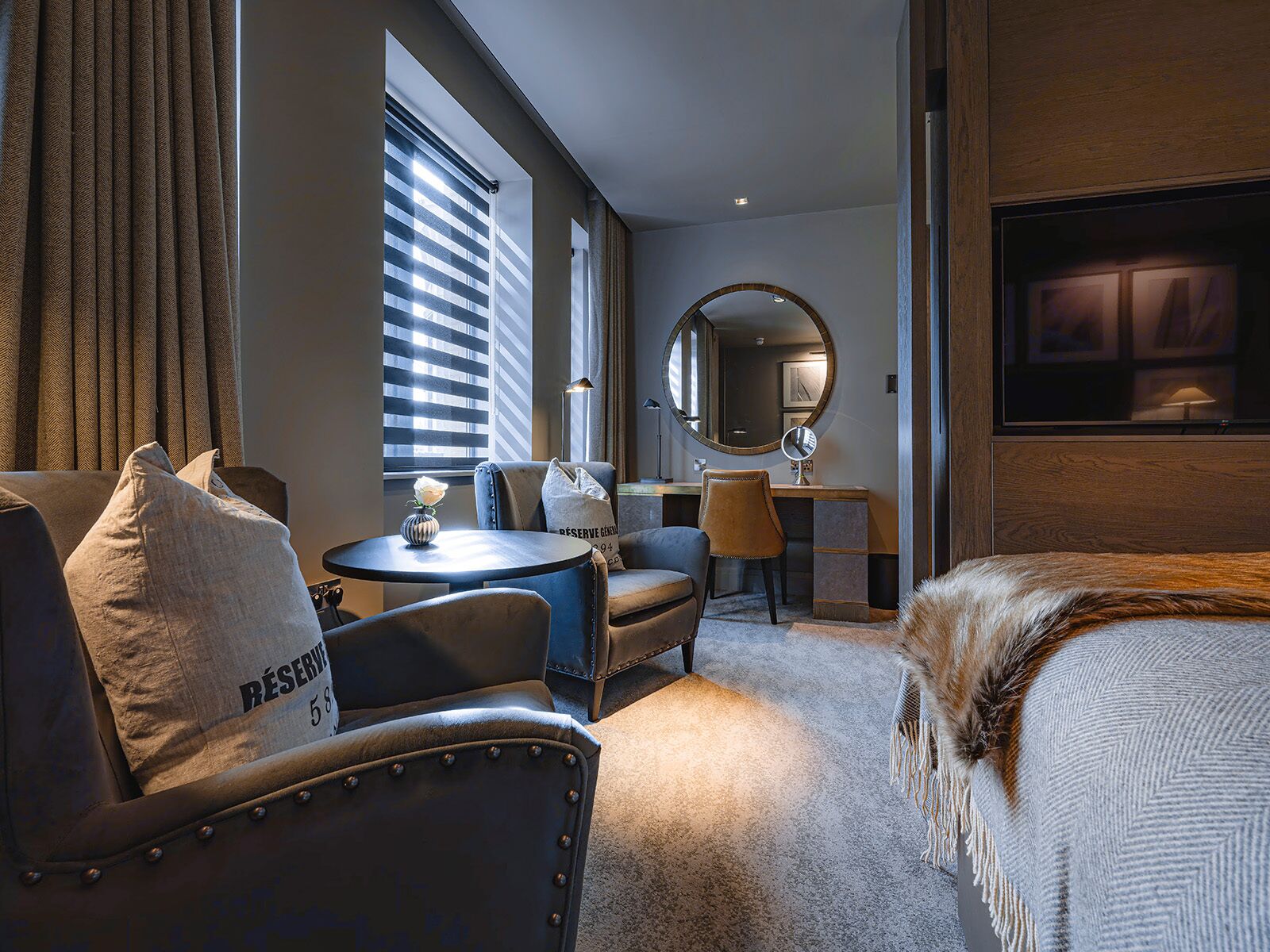 Quarto de hotel com sofá, poltrona, escrivaninha e uma cama.