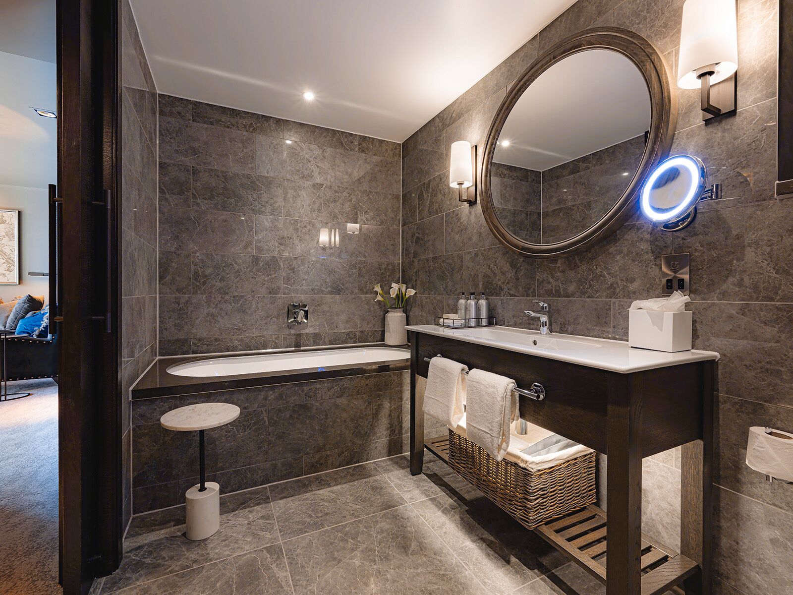 Un baño moderno con un espejo grande, dos lavamanos, un mueble de tocador redondo y un taburete pequeño.