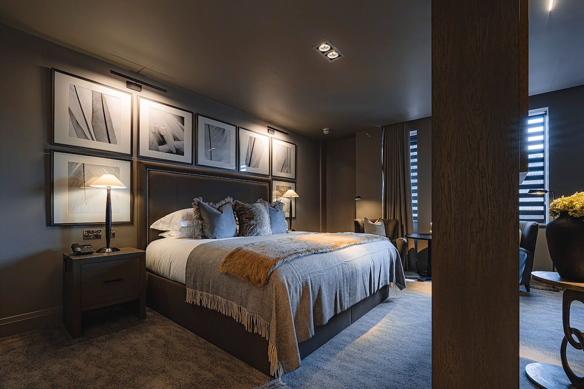 Un dormitorio moderno con una cama grande, varias obras de arte enmarcadas en la pared y una zona de estar acogedora con una mesa y una silla.