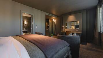 A modern hotel room with a large bed, a desk, a vanity with a mirror, and a bathroom visible through an open door.
