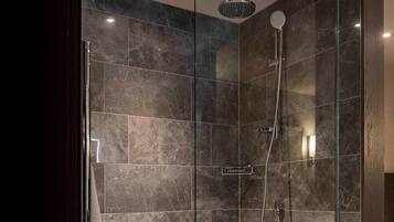 Une douche moderne, dotée d’un pommeau de douche à main et d’un robinet mural, le tout installé sur un mur recouvert de carreaux sombres évoquant le marbre.