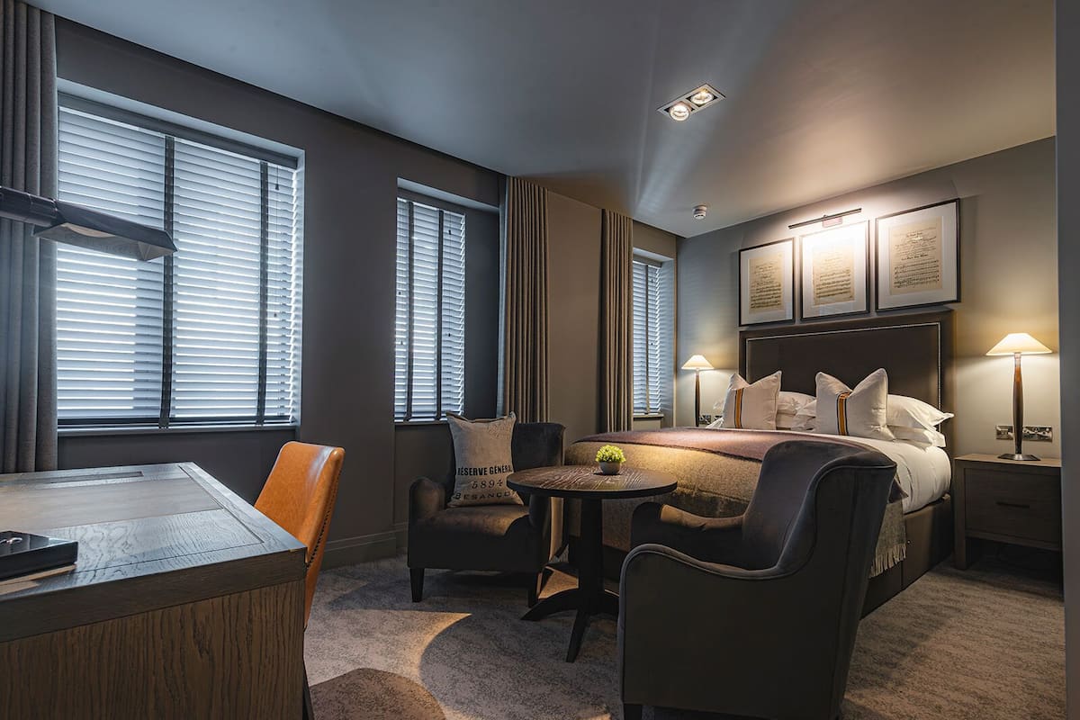 Una habitación de hotel con cama, lámparas de noche, un escritorio y una silla.
