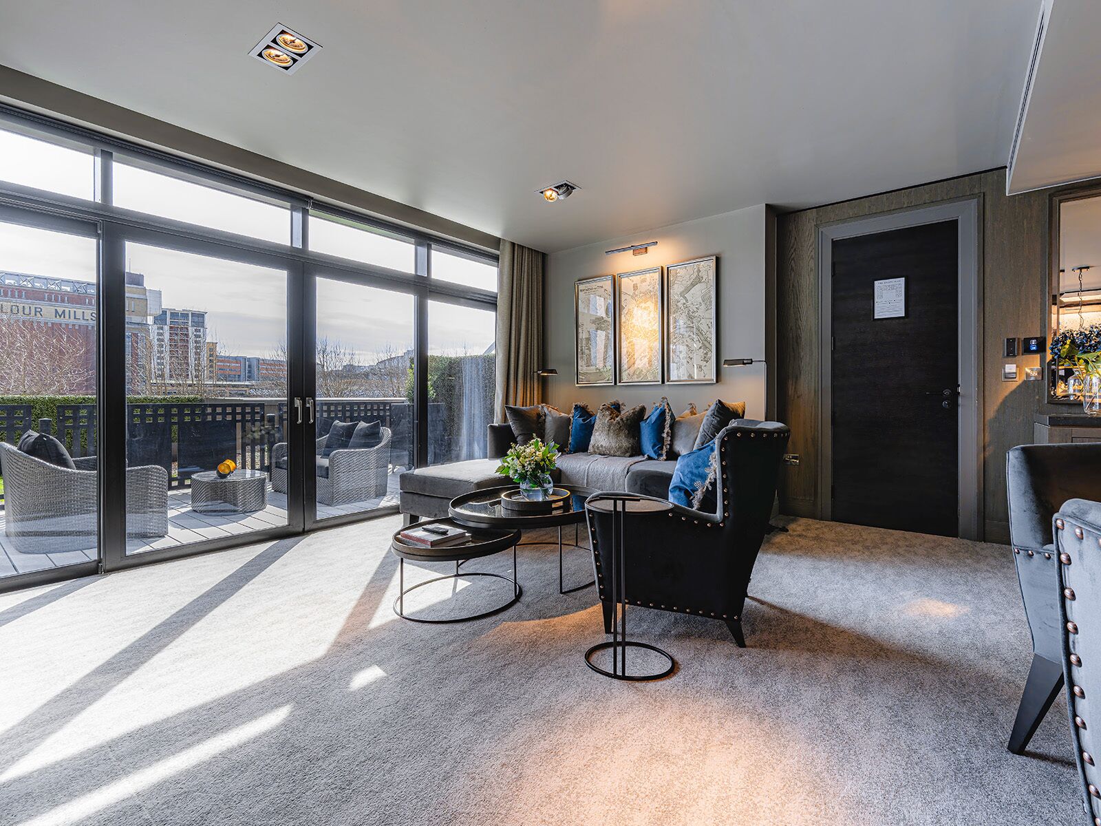 Una sala de estar moderna con un sofá, sillones y una mesita de centro. Amplios ventanales ofrecen vistas a la ciudad.