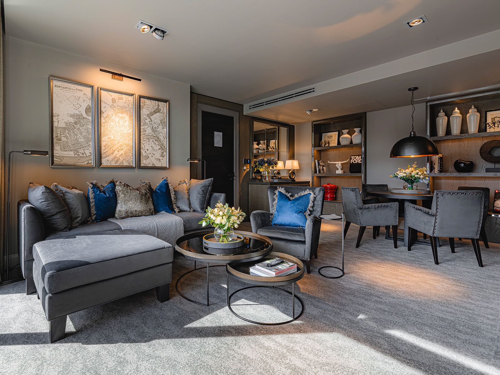 Ein modernes Wohnzimmer mit grauem Sofa, Sesseln, einem Couchtisch und einem Essbereich mit Stühlen und Tisch.
