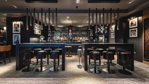 A bar area with multiple stools, a bar counter, and shelves with bottles. - Dakota Newcastle (Newcastle-upon-Tyne)