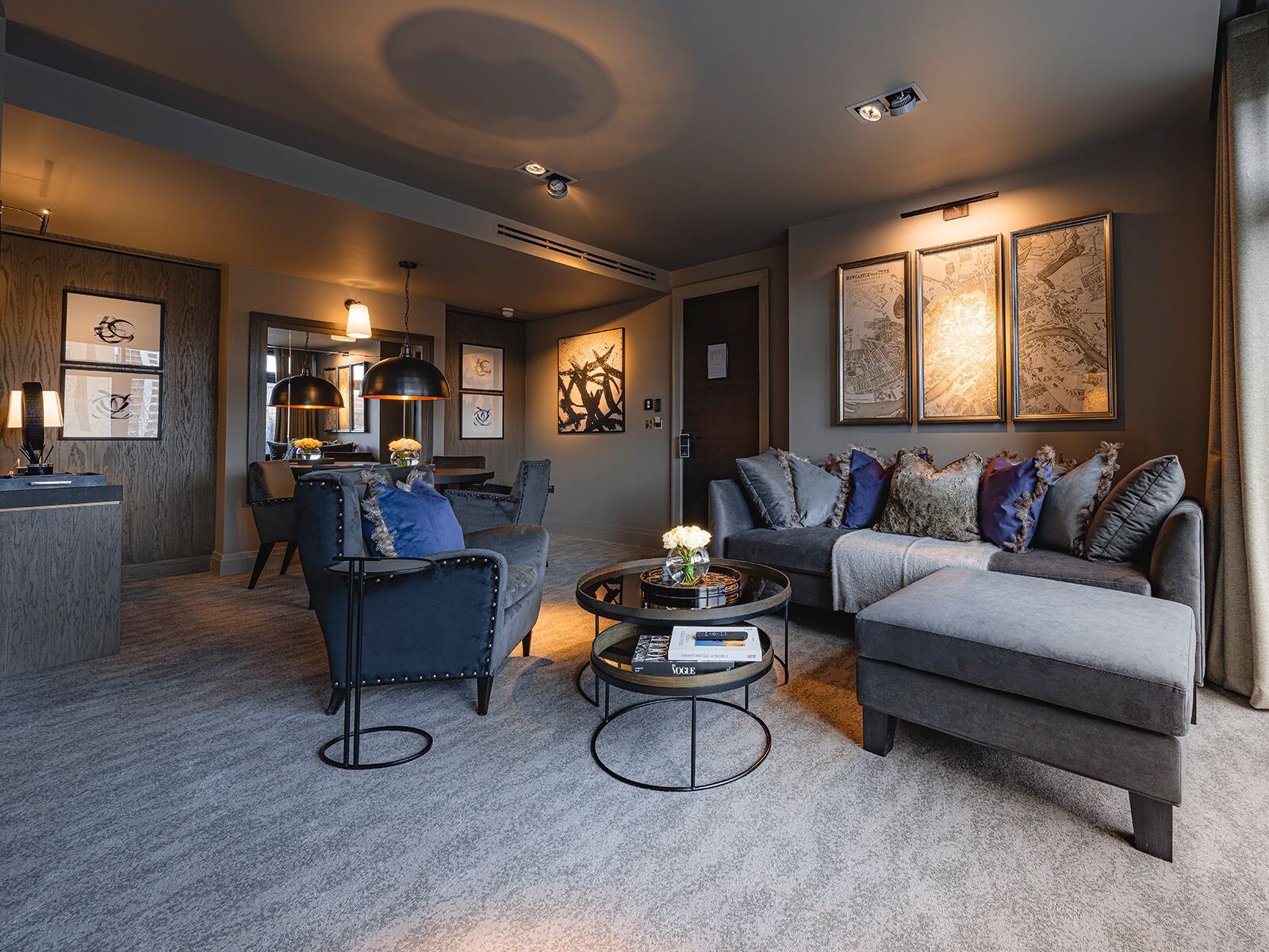 Un salon moderne avec un canapé, un fauteuil et une table basse, agrémenté d’œuvres d’art et comprenant un coin repas à l’arrière-plan.