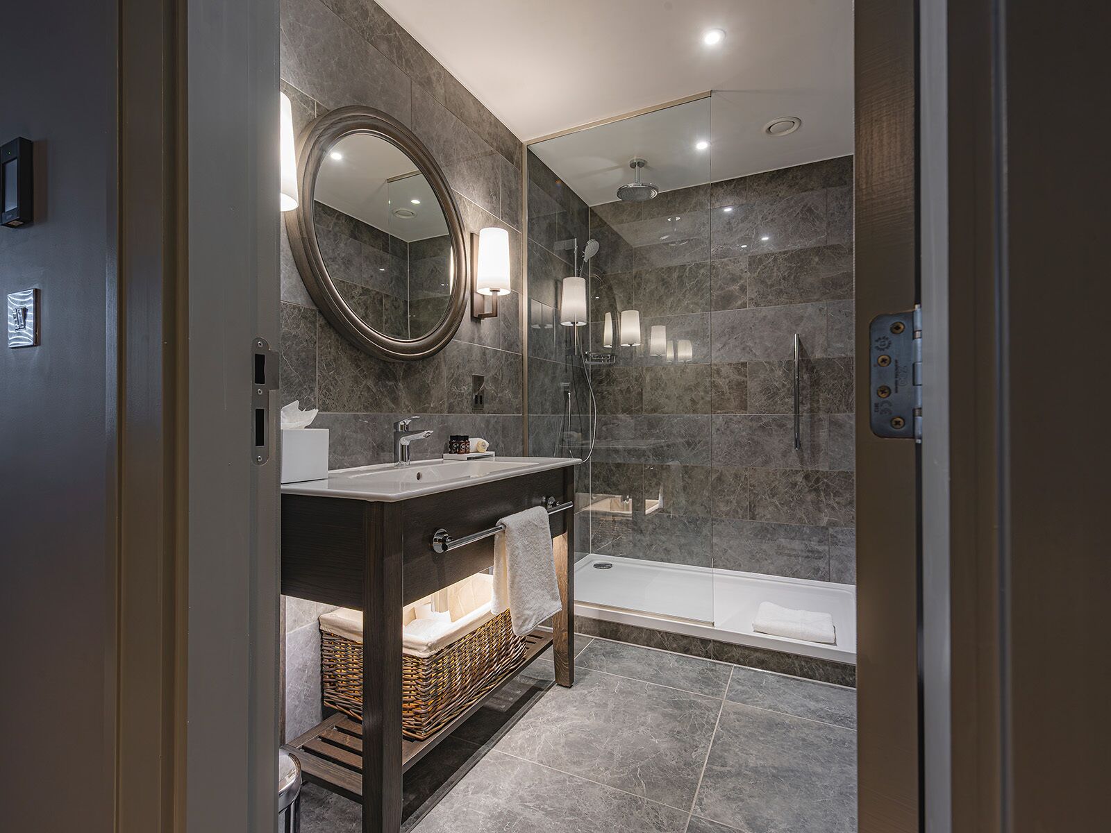 Un baño moderno con tocador de madera oscura, un espejo grande, ducha con mampara de vidrio y una bañera.