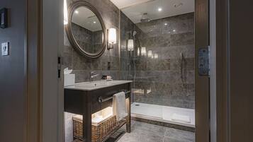 Un baño moderno con tocador de madera oscura, un espejo grande, ducha con mampara de vidrio y una bañera.