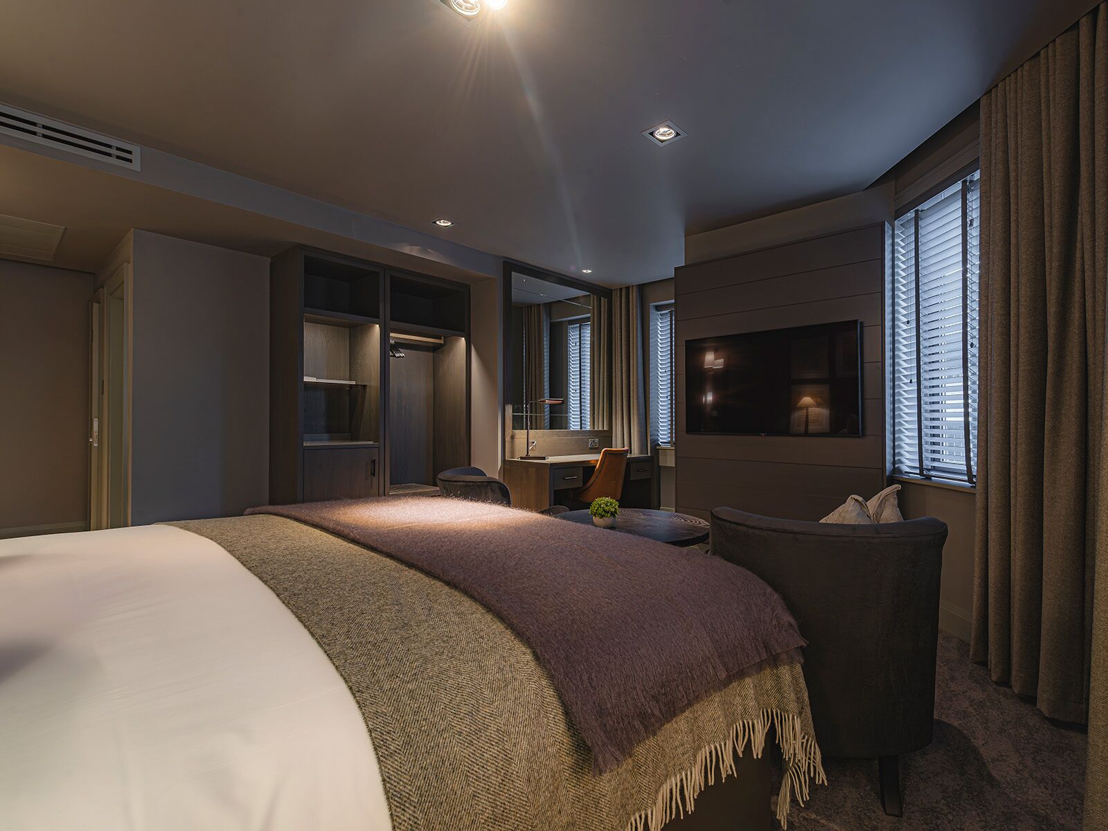 Une chambre d’hôtel avec un grand lit, un bureau avec une chaise, une télévision et une fenêtre avec des rideaux.
