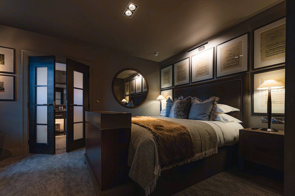 Un dormitorio con una cama grande, una mesita de noche, un espejo y documentos enmarcados en la pared.