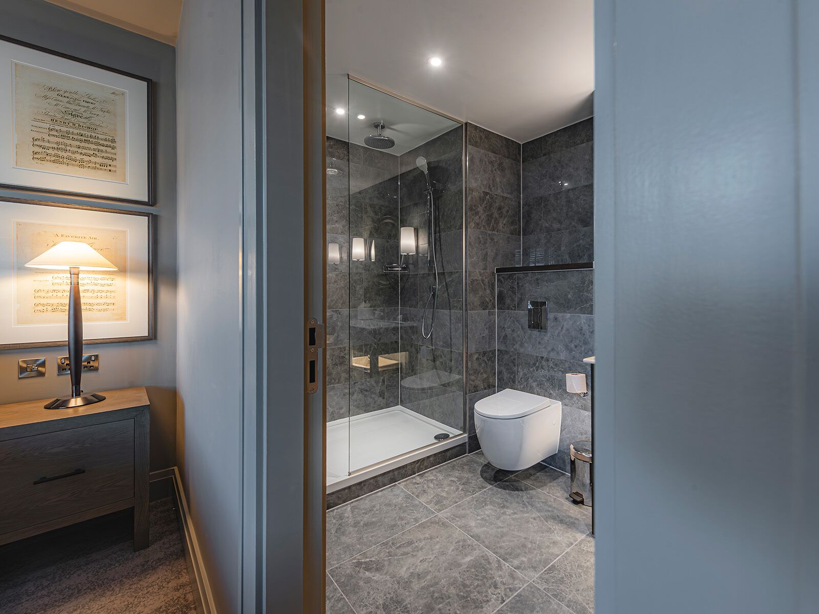 A modern bathroom with a glass-enclosed shower, a white toilet, and a framed document on a wooden table.