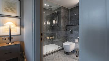 A modern bathroom with a glass-enclosed shower, a white toilet, and a framed document on a wooden table.