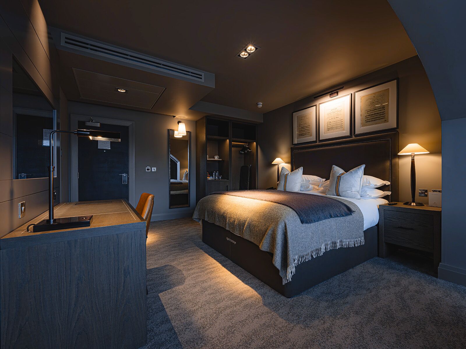 A modern hotel room with a large bed, bedside lamps, a desk, and a mirror.