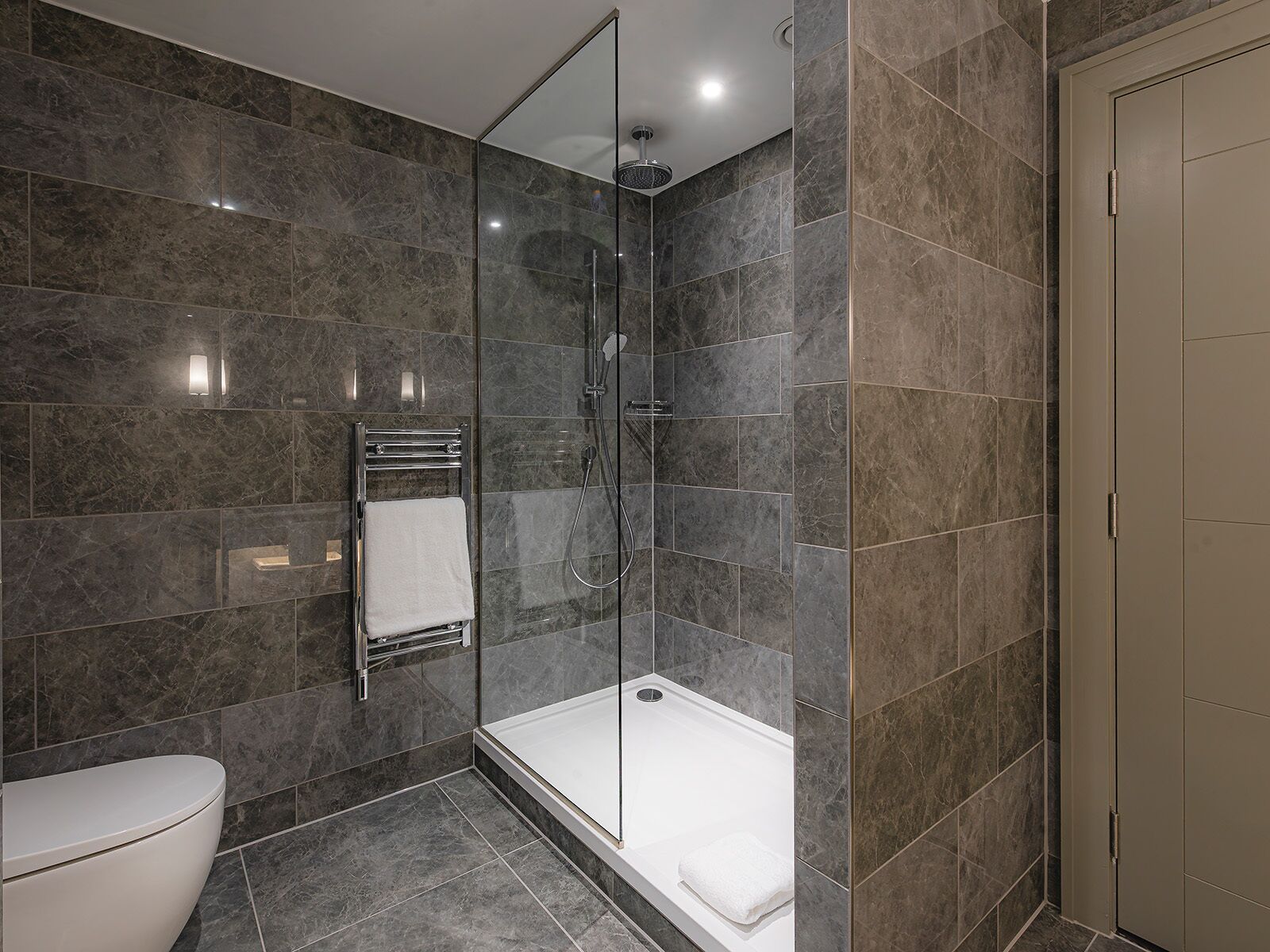 A modern bathroom with a glass-enclosed shower, a white bathtub, and a toilet.