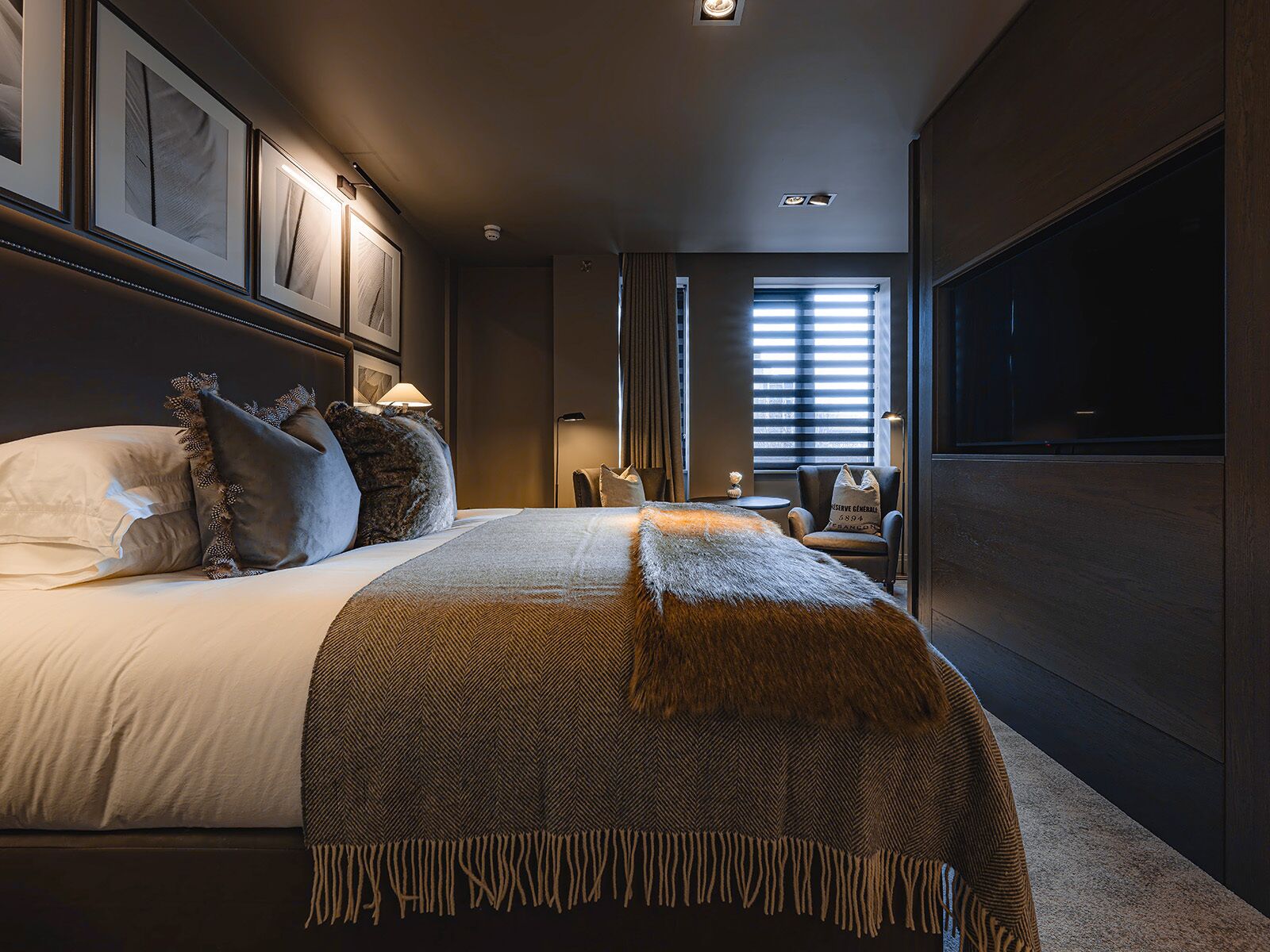 A modern hotel room with a large bed, a flat-screen TV, and a view of the city through the window.