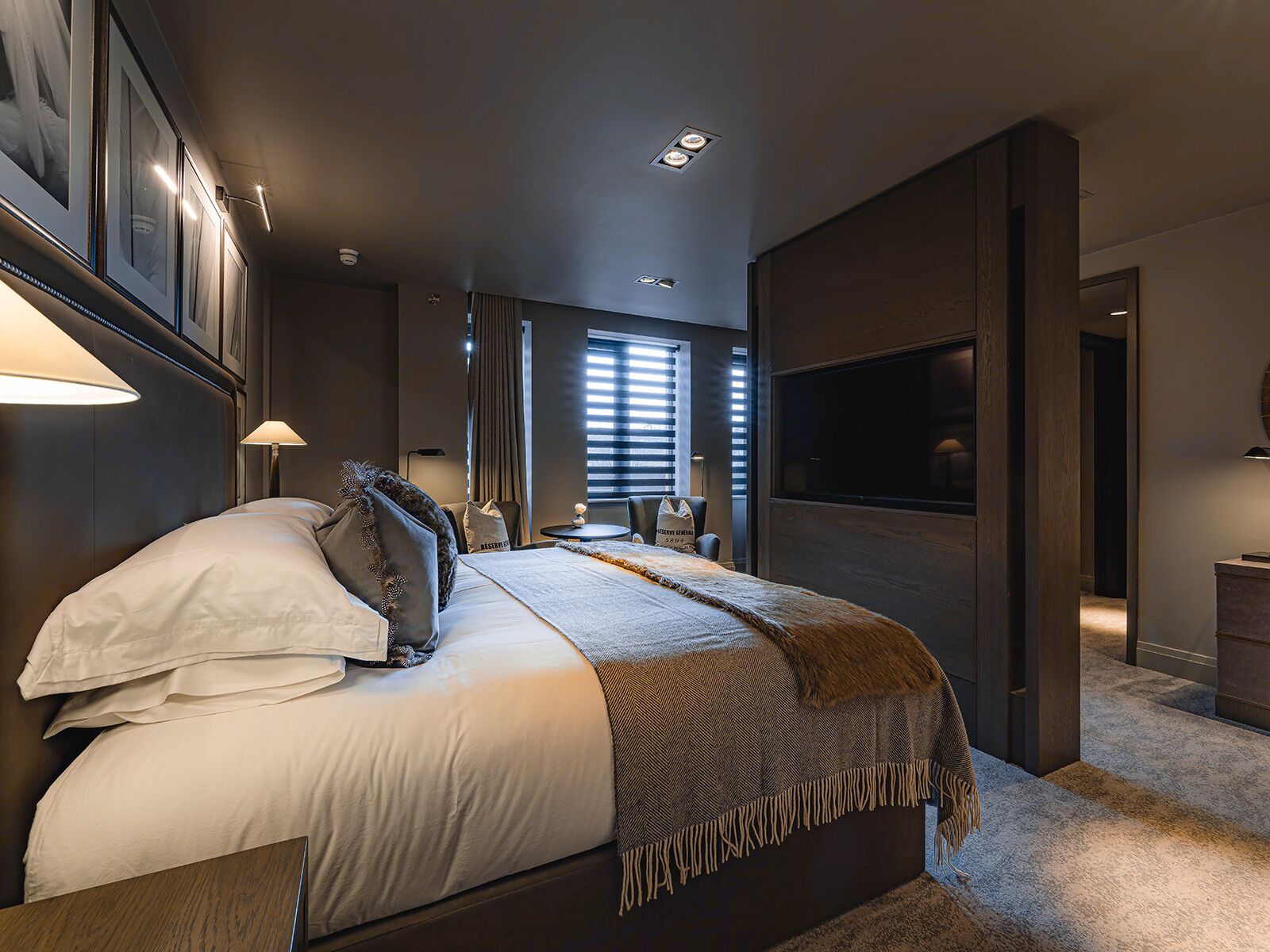 A modern hotel room with a large bed, a flat-screen TV, a desk, and a seating area with a chair and a small table.