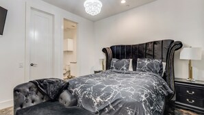 A bedroom with a large bed, a dark upholstered chair, a nightstand, and a chandelier. - Posh Italian home with a rooftop terrace in the heart of Houston! (Houston)