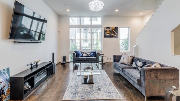 A spacious living room with a large TV, two sofas, a coffee table, and a chandelier. - Posh Italian home with a rooftop terrace in the heart of Houston! (Houston)