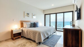 Un dormitorio con cama, mesita de noche y vistas al océano a través de amplias ventanas.