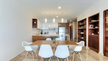 A modern kitchen with white cabinets, a wooden dining table, and white chairs.