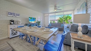 A modern kitchen with a coffee bar, dining area with blue chairs, and a grey sofa.