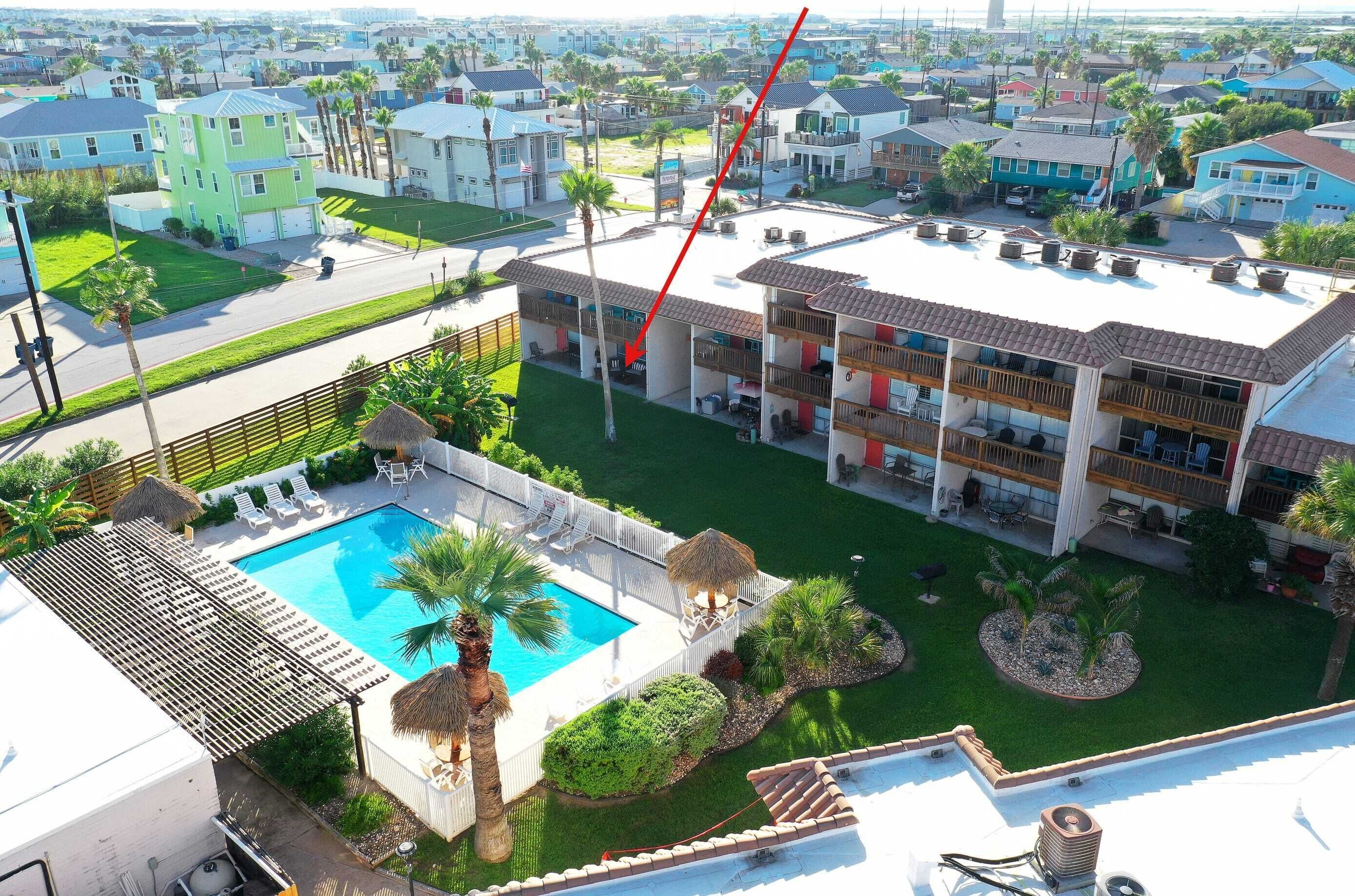 Zona residencial con piscina, patio cercado y un edificio de varios pisos con balcones.