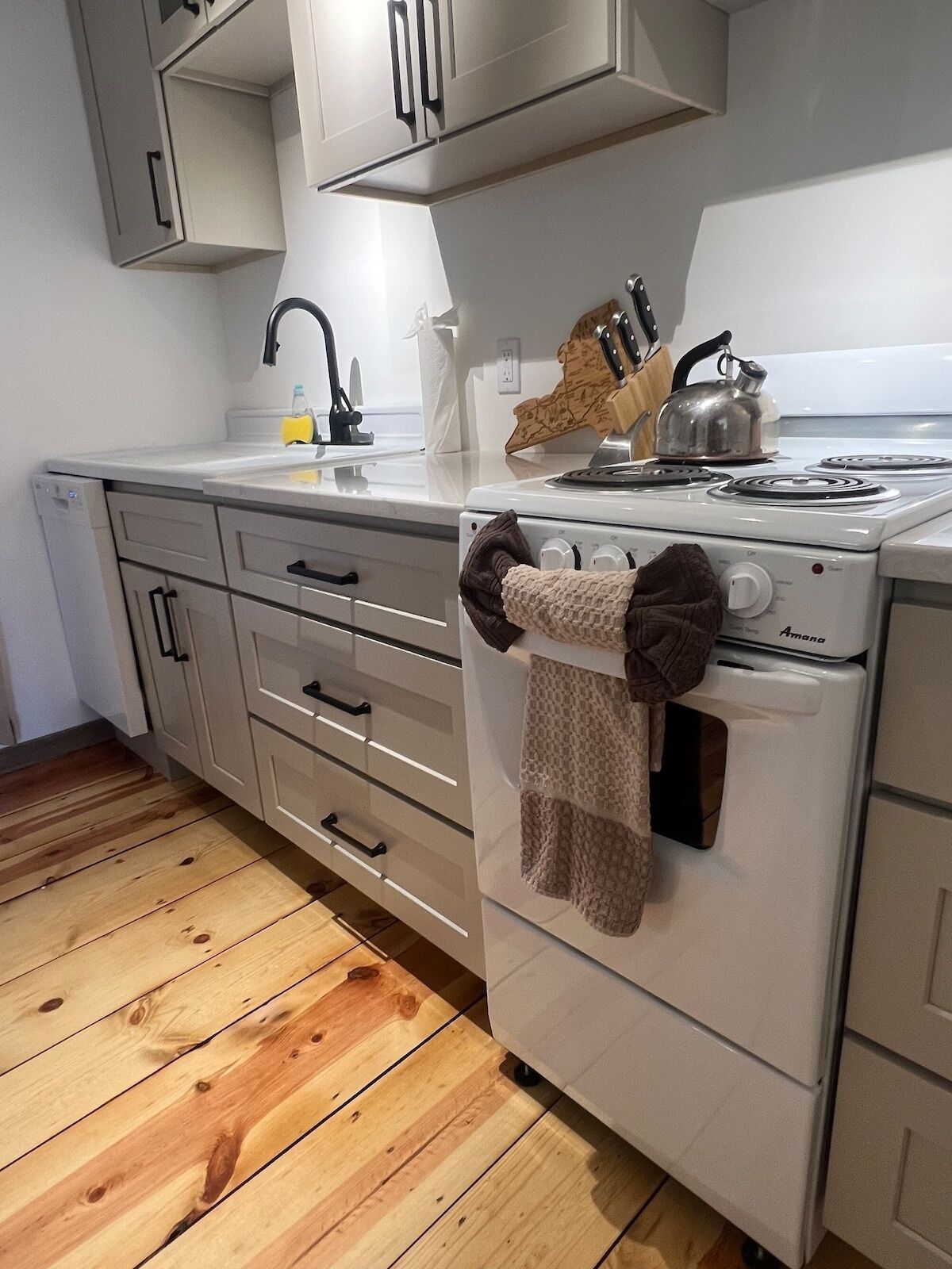 A kitchen with a white stove, wooden flooring, and a knife block on the counter.
