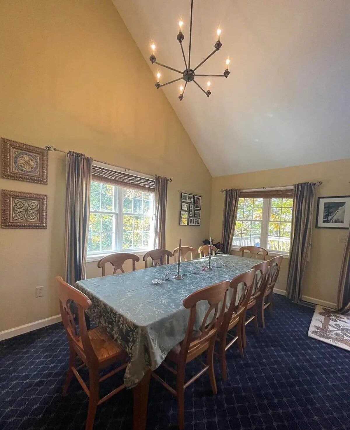 Uma sala de jantar com pé direito alto, um candelabro e uma grande mesa posta para seis.