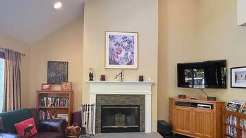 Ein Wohnzimmer mit Kamin, Fernseher, Bücherregal und einer Couch mit Kissen in Form eines Elchs.