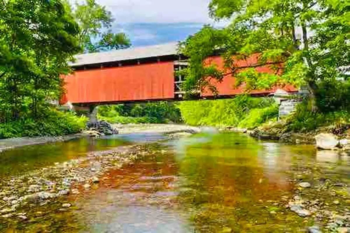 A red covered bridge over a clear stream surrounded by lush greenery.