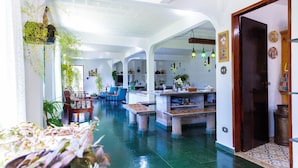 A spacious, well-lit interior with a central dining area, multiple seating arrangements, and hanging plants. - Sitio Natureza piscina e churrasqueira (Ibiuna)