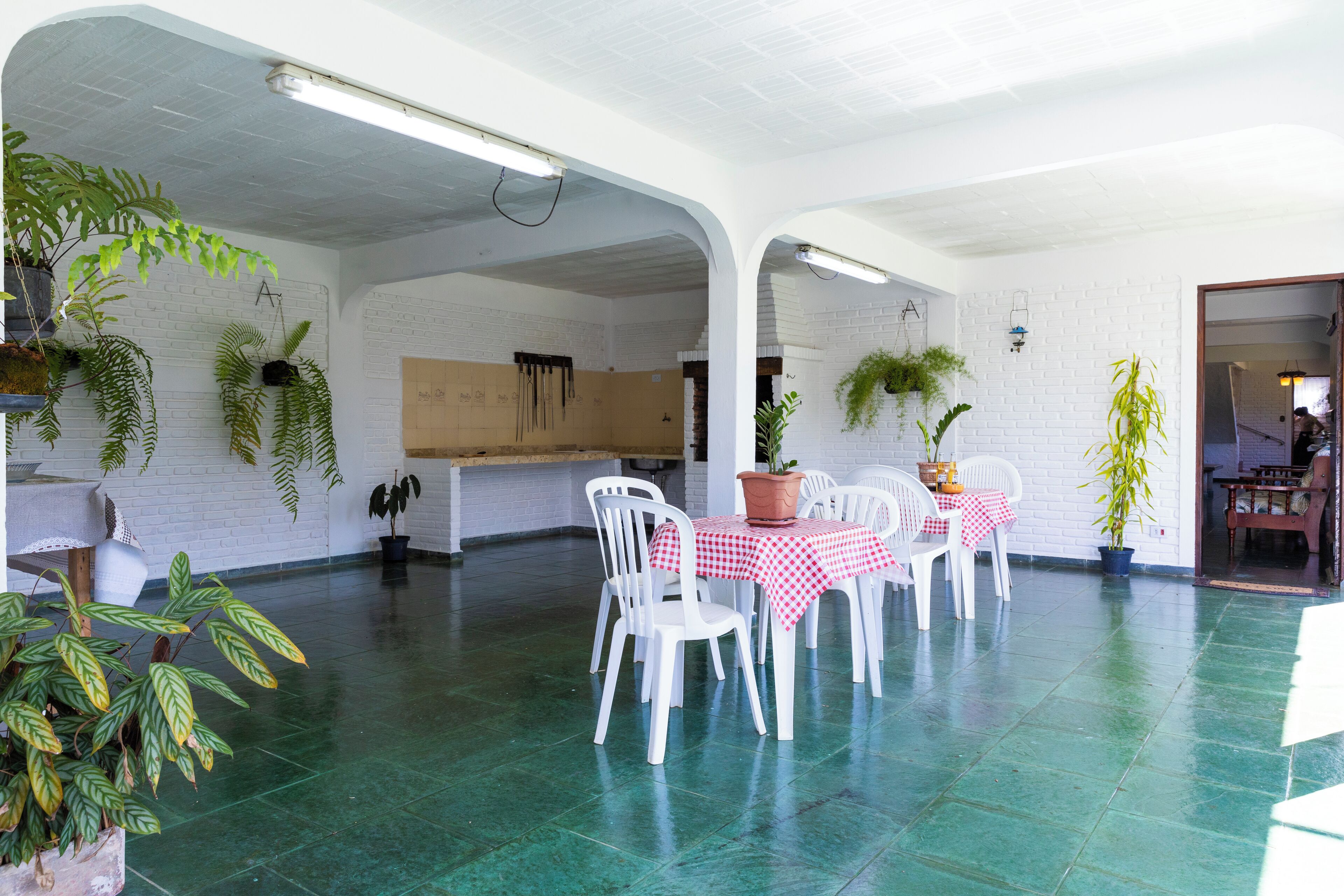 A spacious indoor area with white brick walls, green flooring, and white chairs around a table with a red and white checkered tablecloth.