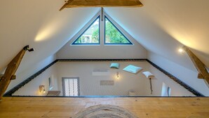 Un dormitorio tipo loft con techo inclinado, suelo de madera y ventana de malla.