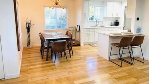 A modern kitchen with white cabinets, a central island, and a dining area with a wooden table and chairs. - Buena Park Modern Home/Knott's/Disney/Beach

 (Buena Park)