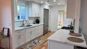 A modern kitchen with white cabinets, a stainless steel refrigerator, and a large island with a woven placemat. - Buena Park Modern Home/Knott's/Disney/Beach

 (Buena Park)