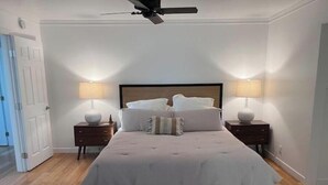 A bedroom with a large bed, two bedside tables with lamps, a ceiling fan, and a door to the left. - Buena Park Modern Home/Knott's/Disney/Beach

 (Buena Park)