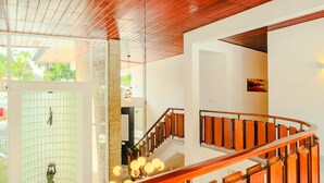 Un intérieur moderne avec un escalier en bois, une statue et une vue sur la verdure à l’extérieur.