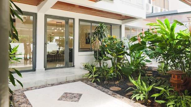 Une maison moderne dotée d’un patio agrémenté d’un sol en pierre, de plantes en pot et d’une petite lanterne décorative.